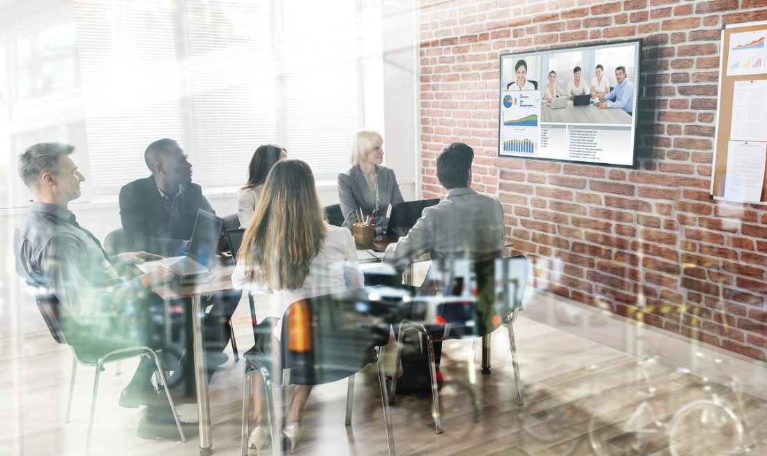 People sitting at a table and talking with video participants on TV installed on the wall. This represents the Shure Logitech Collaboration.