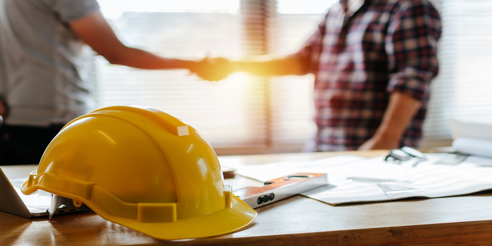 Construction work hat sitting on table in front of two AV subcontractors shaking hands.