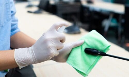 worker hand wearing gloves using disinfectant spray and cloth to clean microphone in conference room to prevent covid-19 or coronavirus infection. new normal and social distancing concept