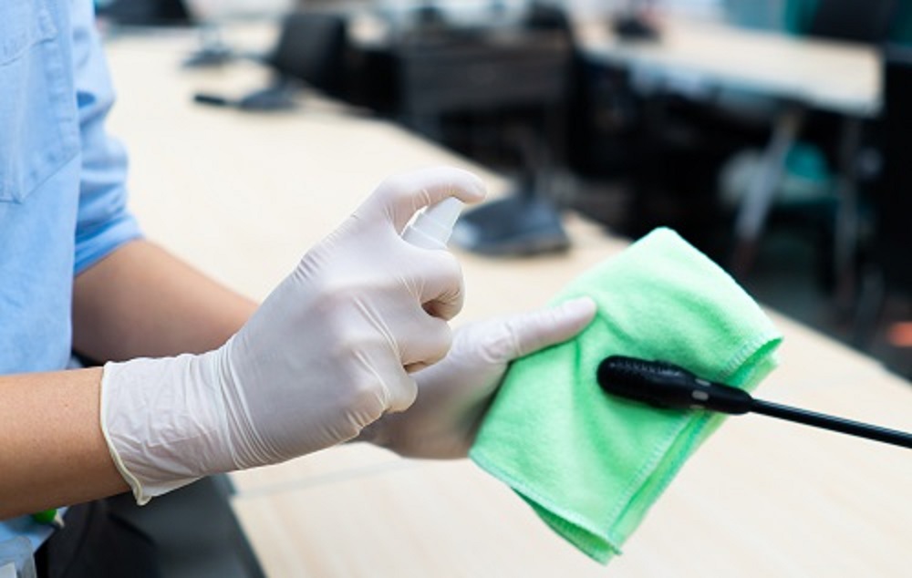 worker hand wearing gloves using disinfectant spray and cloth to clean microphone in conference room to prevent covid-19 or coronavirus infection. new normal and social distancing concept