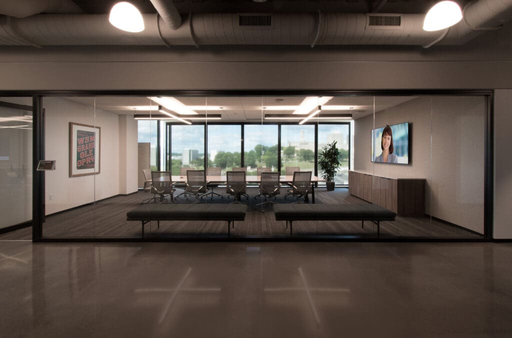 Wide view of an office at HealthStream's headquarters. It has a glass exterior. There is a long table with chairs on either side sits in the center while a display screen can be seen on the right wall.