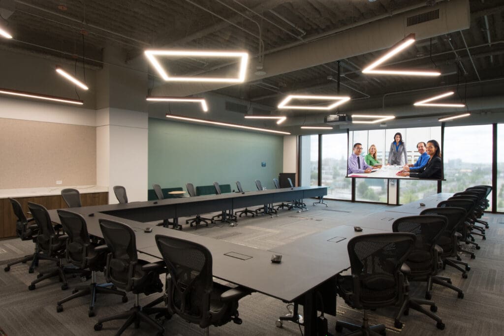 Side view of room at HealthStream Headquarters. There is a U-shaped large conference table with chairs all around. The room also has a glass wall with a display screen mounted on it.