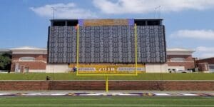 Field goal post of football stadium with a scoreboard behind it.