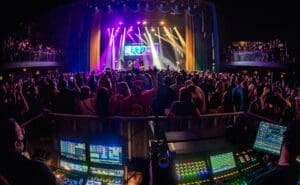 A huge crowd in front of a stage. In the forefront, there is an audio system