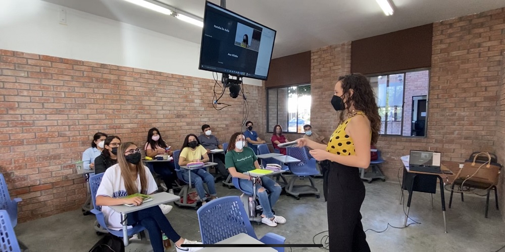 Masked professor addressing a classroom at La Salle Laguna. Above the professor is a screen showcasing remote students