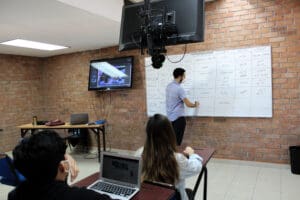 Professor demonstrating on whiteboard in a packed classroom