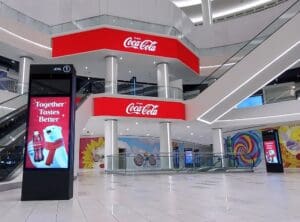 Mall interiors with an escalator with signage boards displaying the Coca-Cola brands