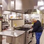 Chef in a black shirt standing in an empty kitchen. The chef is attempting to turn on the stove.