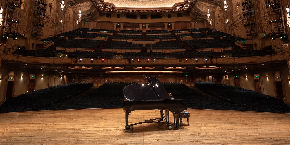 A piano on a stage with empty seats in the background. The venue is fitted with Meyer Sound Constellation