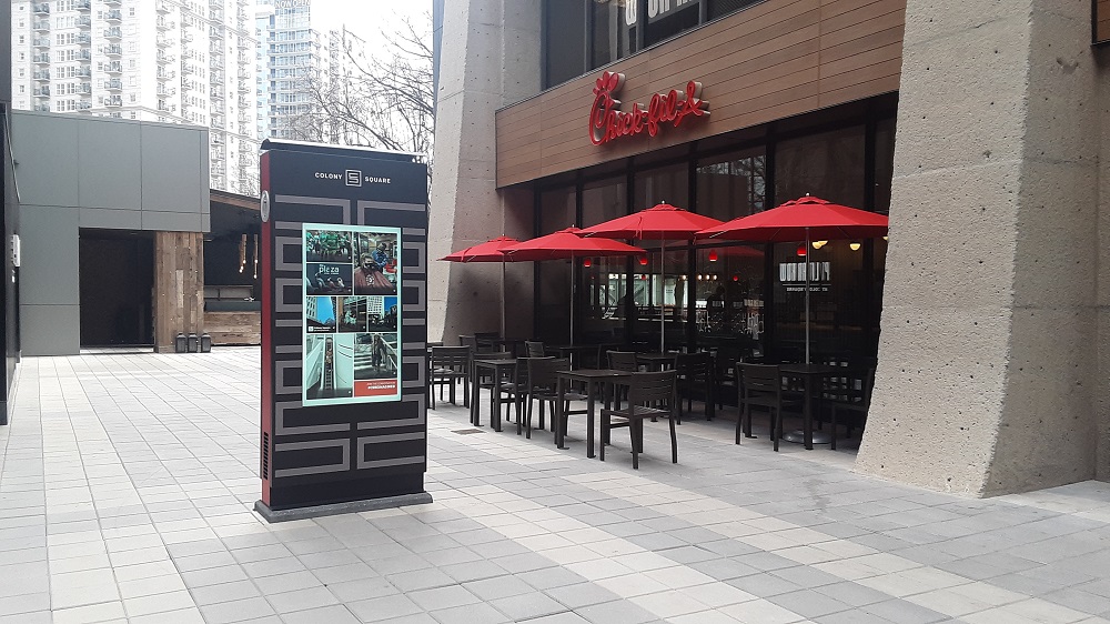 Digital Kiosk with Colony Square written on top of the screen. The kiosk stands next to a restaurant.