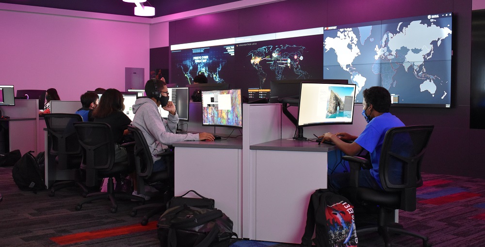 NEISD Cyber Training room with students working on laptops. A video wall with a world map hangs behind powered by RGB Spectrum Galileo processors