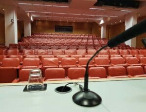 Closeup of table with mic stand. Across the table are empty auditorium seats.