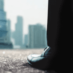 Close-up of person's shoes with blurred buildings in the background. Image symbolizes the state of the AV industry.