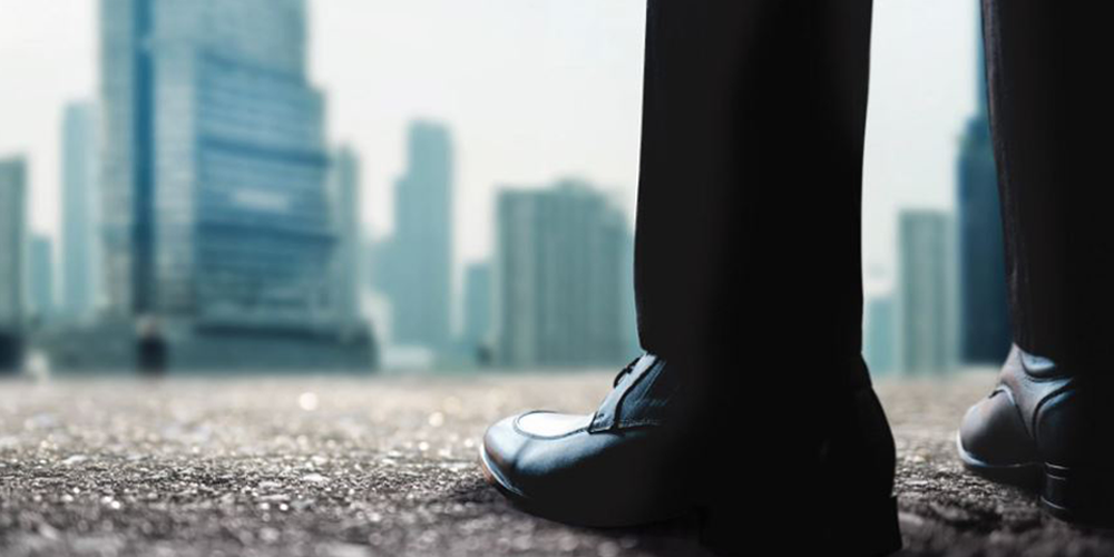 Close-up of person's shoes with blurred buildings in the background. Image symbolizes the state of the AV industry.