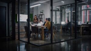 Long shot of person speaking to people seated in an office room.