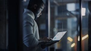 Person standing and working on a laptop. Face is illuminated by the laptop backlight.