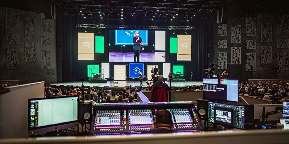 Person sitting with DiGiCo console in auditorium at Seacoast Church. In front, an audience is watching a speaker on stage.