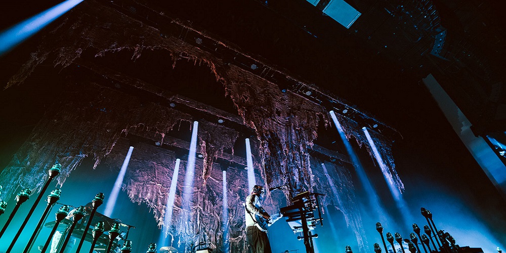 Upward shot of Bon Iver playing at YouTube Theater fitted with L-ISA technology. The stage is lit up with blue lighting while Justin Vernon plays the guitar.