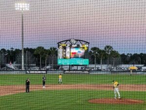 Netted view of UFC Baseball Stadium where players are lined up in front of a videoboard.