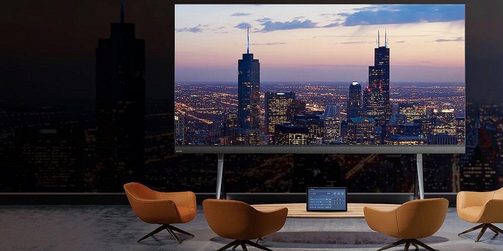 Mockup of MAXHUB's LM138A07TAA display in front of a conference table and chairs.