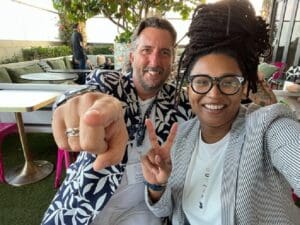 Two people laughing at camera. One person is pointing to the camera while the other makes a peace sign.