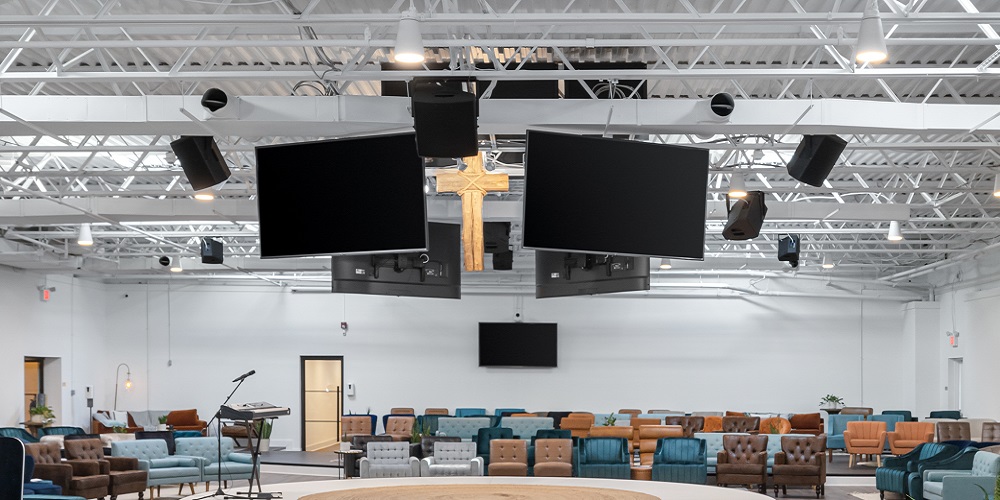 Bose speakers provided by Whitaker Technologies hang from ceiling in room with blue accent chairs.