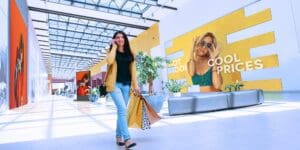 Person with shopping bags walking past a 41-inch LED panel videowall. On the videowall is a mock ad for sunglasses.