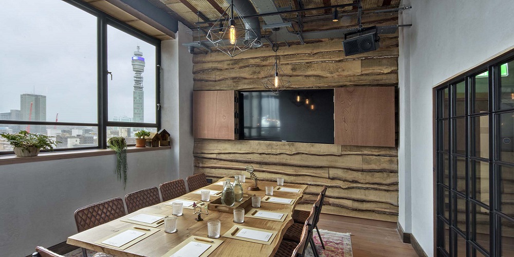 Restaurant in Treehouse London with KV2 speakers hanging from the ceiling. A large dining table with chairs and crockery sit in the center of the room.