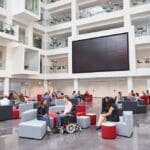 Students socialising under AVoIP screen in atrium at university education campus