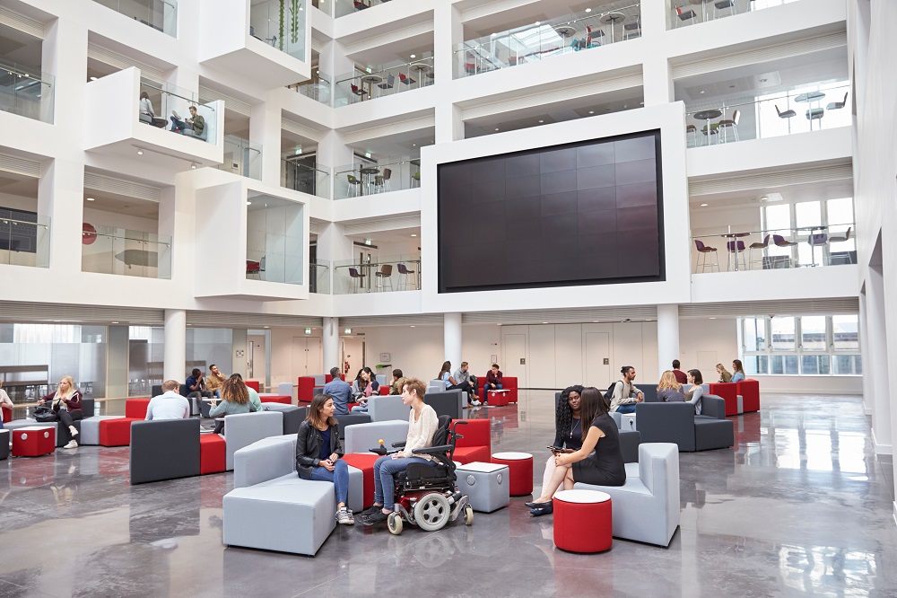 Students socialising under AVoIP screen in atrium at university education campus