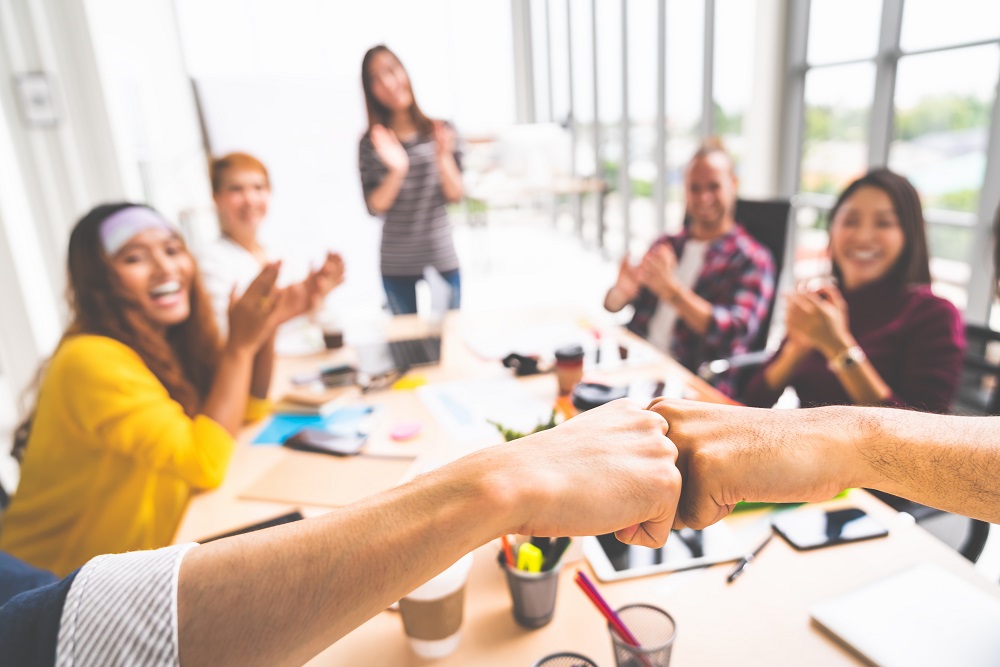 Coworkers fist bump in team meeting, happy colleagues clapping hands. Teamwork cooperation, company morale, company culture