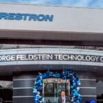 Crestron George Feldstein Technology Center with blue and white balloons decorating the front door. There is also a podium in front of the building where a person is holding a mic.