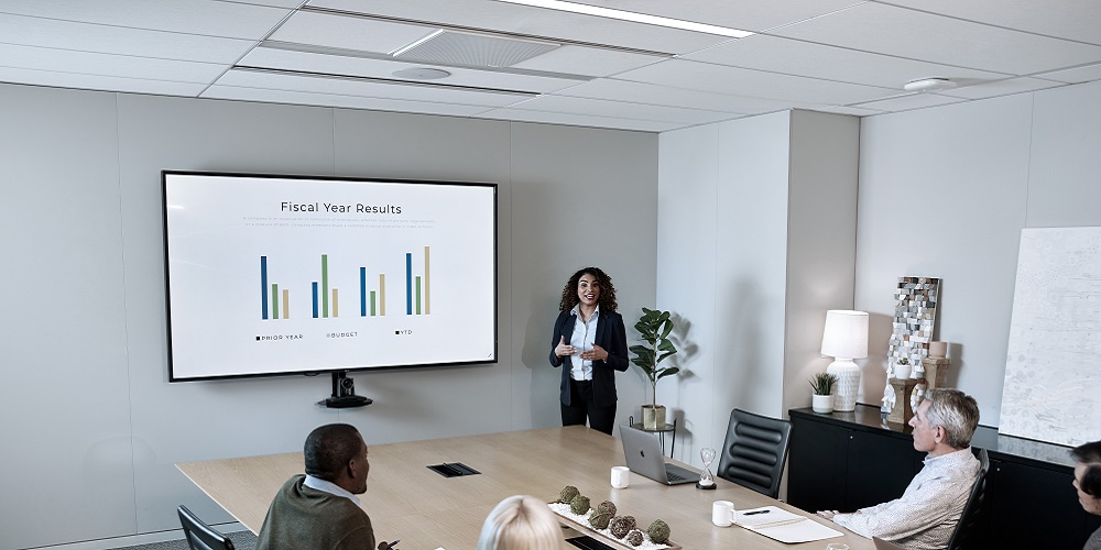 Shure MXA920 discreetly placed on ceiling of conference room. Inside the room, professionals are holding a meeting at a long table.