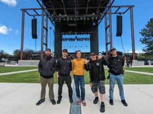 L-Acoustics team posing in front of speaker system on stage.