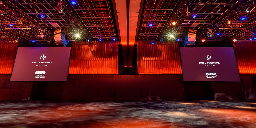 The Londoner logo on projection screen in room bathed in red lights.