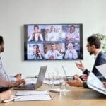 Workers in a conference room with a screen showing remote participants on Zoom.