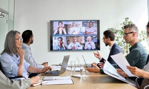 Workers in a conference room with a screen showing remote participants on Zoom.