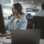 Diverse Office: Portrait of Talented Indian Girl IT Programmer Working on Desktop Computer in Friendly Multi-Ethnic Environment. Female Software Engineer Wearing Glasses Develop Inspirational App