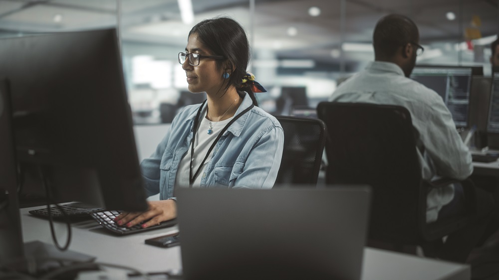 Diverse Office: Portrait of Talented Indian Girl IT Programmer Working on Desktop Computer in Friendly Multi-Ethnic Environment. Female Software Engineer Wearing Glasses Develop Inspirational App