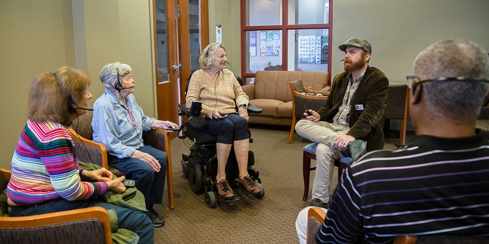 Senior citizens sitting in a circle at Crown Center and wearing ListenTALK headsets.