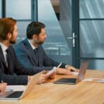 people sitting around conference table conducting hybrid meeting