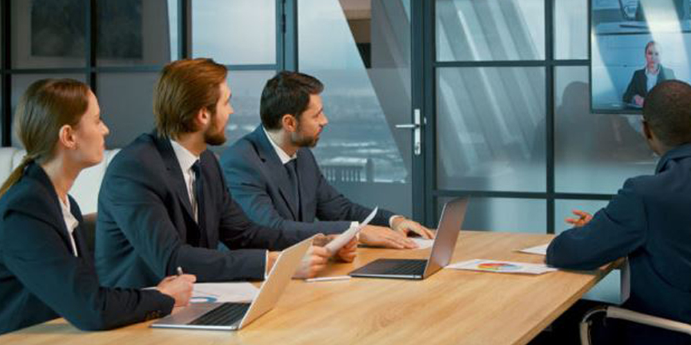 people sitting around conference table conducting hybrid meeting