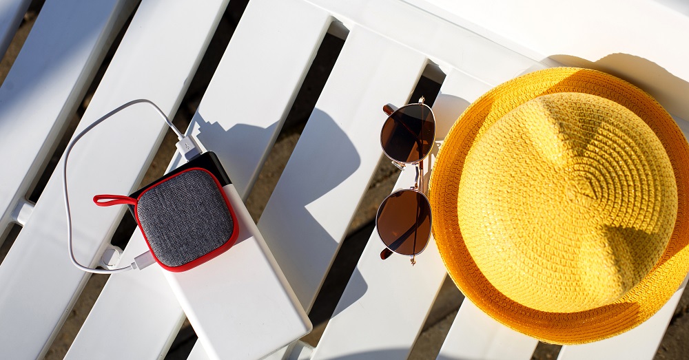 Music portable speaker is charged from the power bank via usb on a deck chair near the pool with beach accessories.