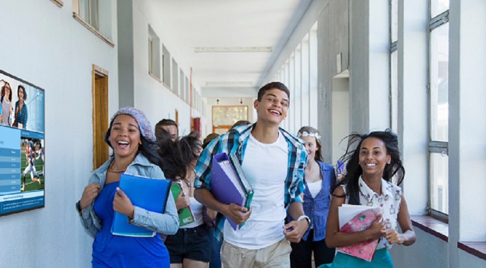 Students running down a campus hall and following signs on a Samsung digital display.