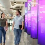 two people walking down hallway lined with LG displays