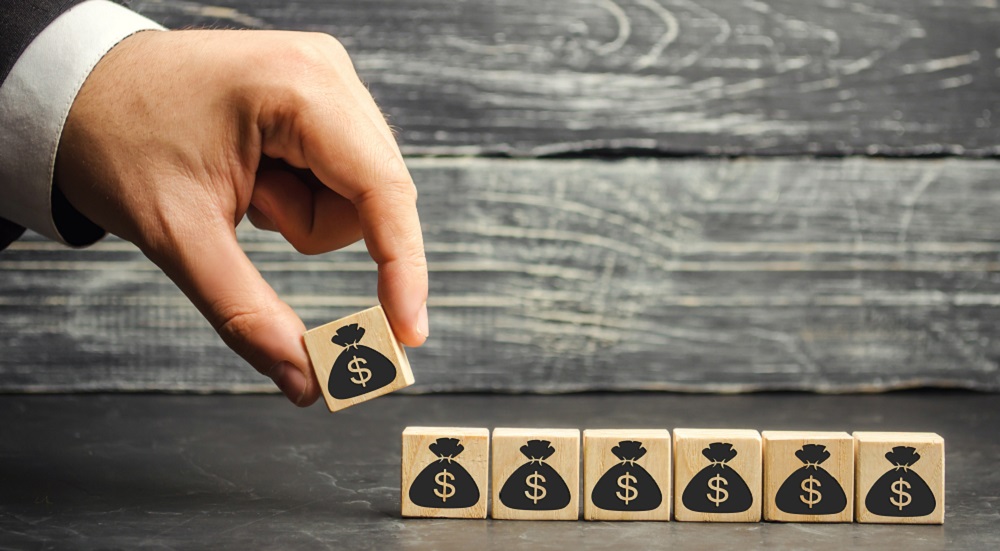 Person's hand placing a block with a money bag icon next to other similar blocks to symbolize business growth for AV integrators.