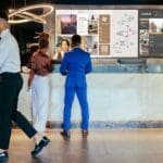 Couple checking into hotel front desk with digital signage videowall in background