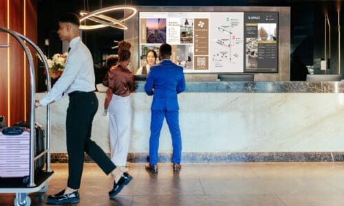 Couple checking into hotel front desk with digital signage videowall in background