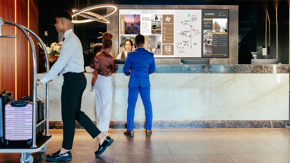 Couple checking into hotel front desk with digital signage videowall in background