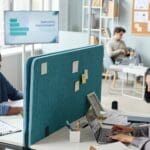 Side view portrait of two people working in office separated by partition wall.